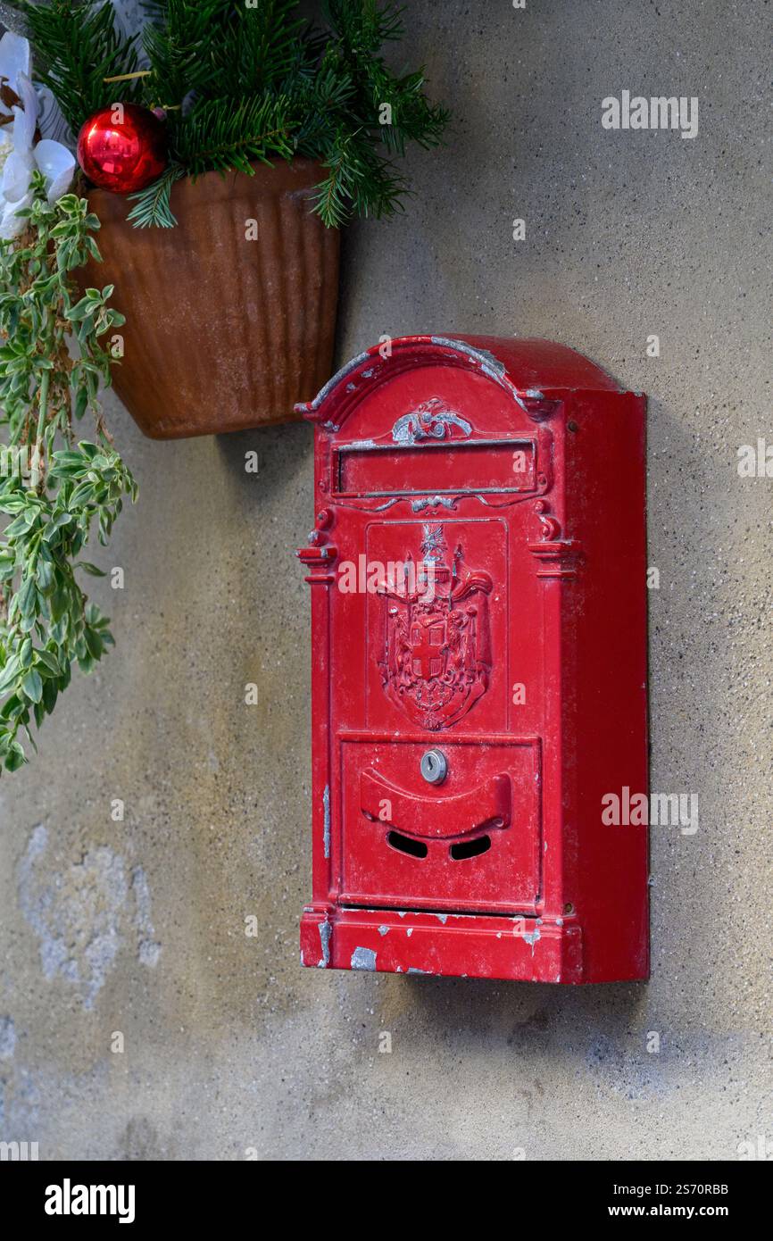 Cassetta postale rossa decorata applicata su una parete in stucco beige chiaro, adornata con vegetazione natalizia e un festoso ornamento rosso. Foto Stock