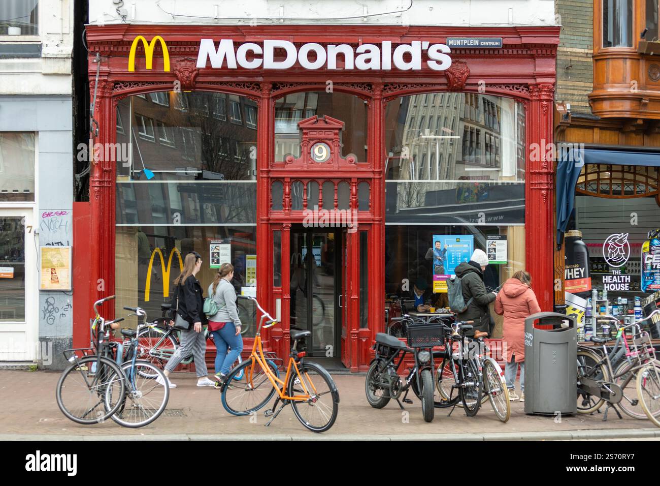 Le biciclette sono parcheggiate davanti al McDonald's Restaurant, edificio in stile retrò, in una trafficata via dello shopping a Muntplein, nel centro di Amsterdam. Foto Stock