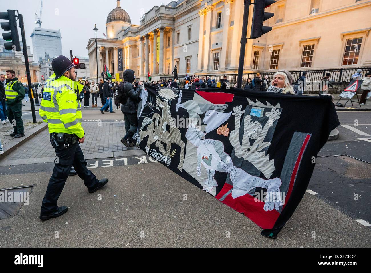 Londra, Regno Unito. 18 gennaio 2025. Una donna che porta una versione arazzo di Guernica viene arrestata apparentemente per aver violato la sezione 14 dell'atto di ordine pubblico, nonostante gli sforzi di suo figlio di intervenire - la marcia alla fine parte. Ma è di nuovo bollito a Trafalgar Square da cordoni di polizia ad ogni angolo - la 23a marcia Nazionale per la Palestina a Londra, affermando a Whitehall e dirigendosi verso la BBC, nonostante le restrizioni della polizia. I manifestanti chiedono che la Gran Bretagna ponga fine alla sua "complicità nel genocidio di Israele in Palestina e nei bombardamenti e nell'invasione terrestre del Libano”. Crediti: Guy Bell/Alamy Live News Foto Stock