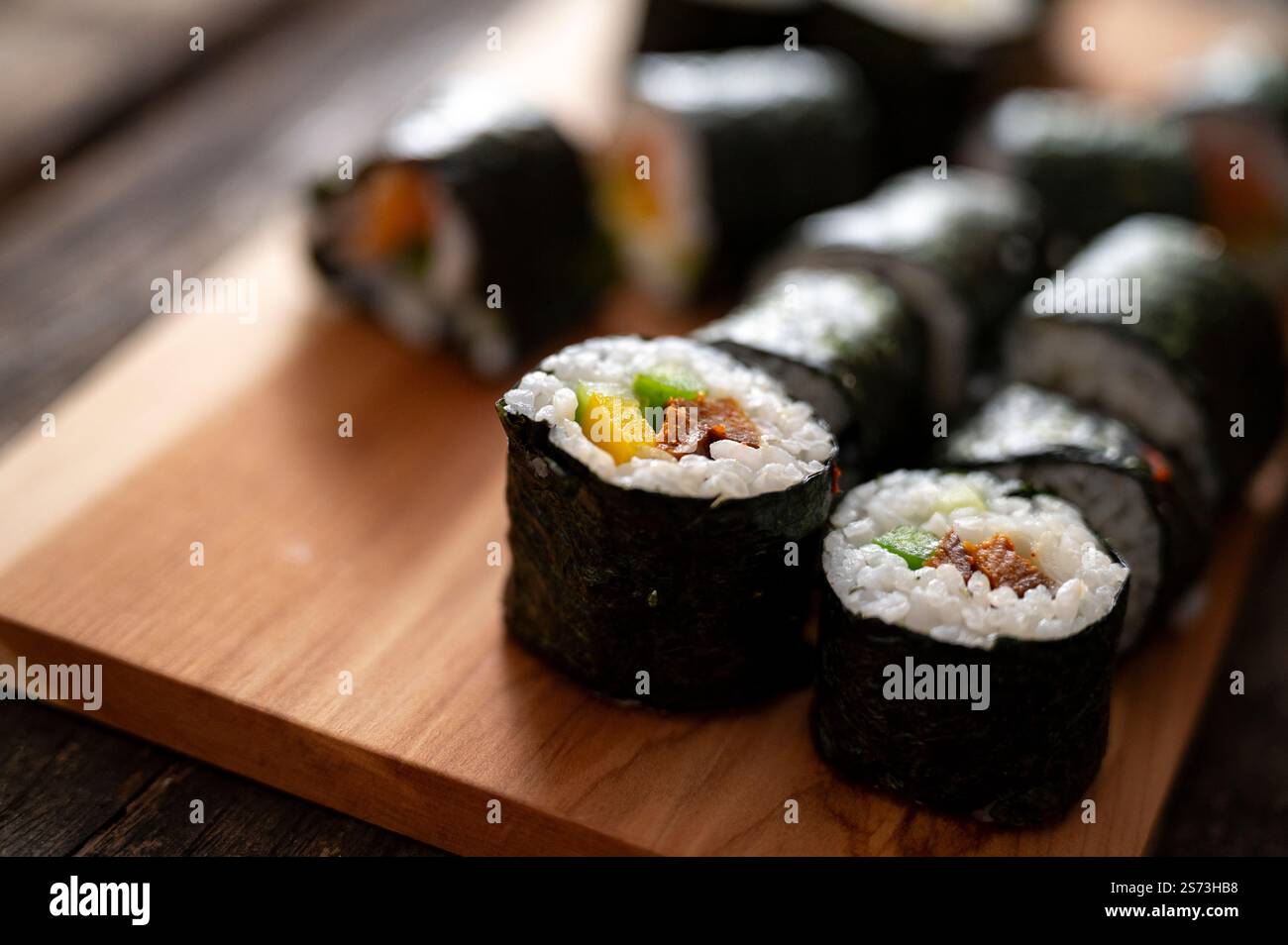 Primo piano di sushi ben disposti, ripieni di verdure e riso, posti su una tavola di legno, pronti per essere serviti. Foto Stock