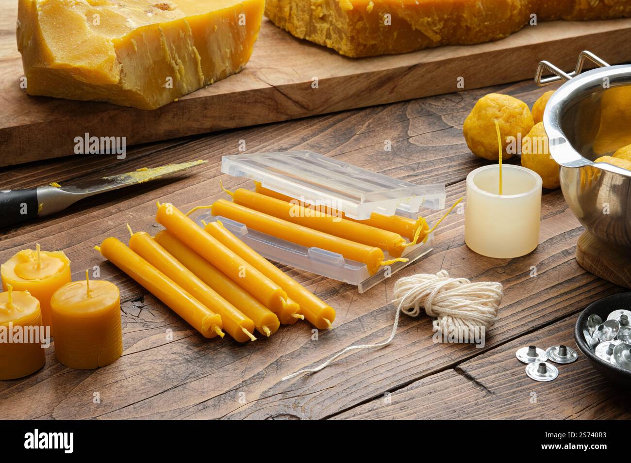 Cera d'api, stampi, stoppini, stoppini metallici, melting pot, coltello e utensili per realizzare candele naturali fatte a mano su una superficie rustica in legno. Foto Stock