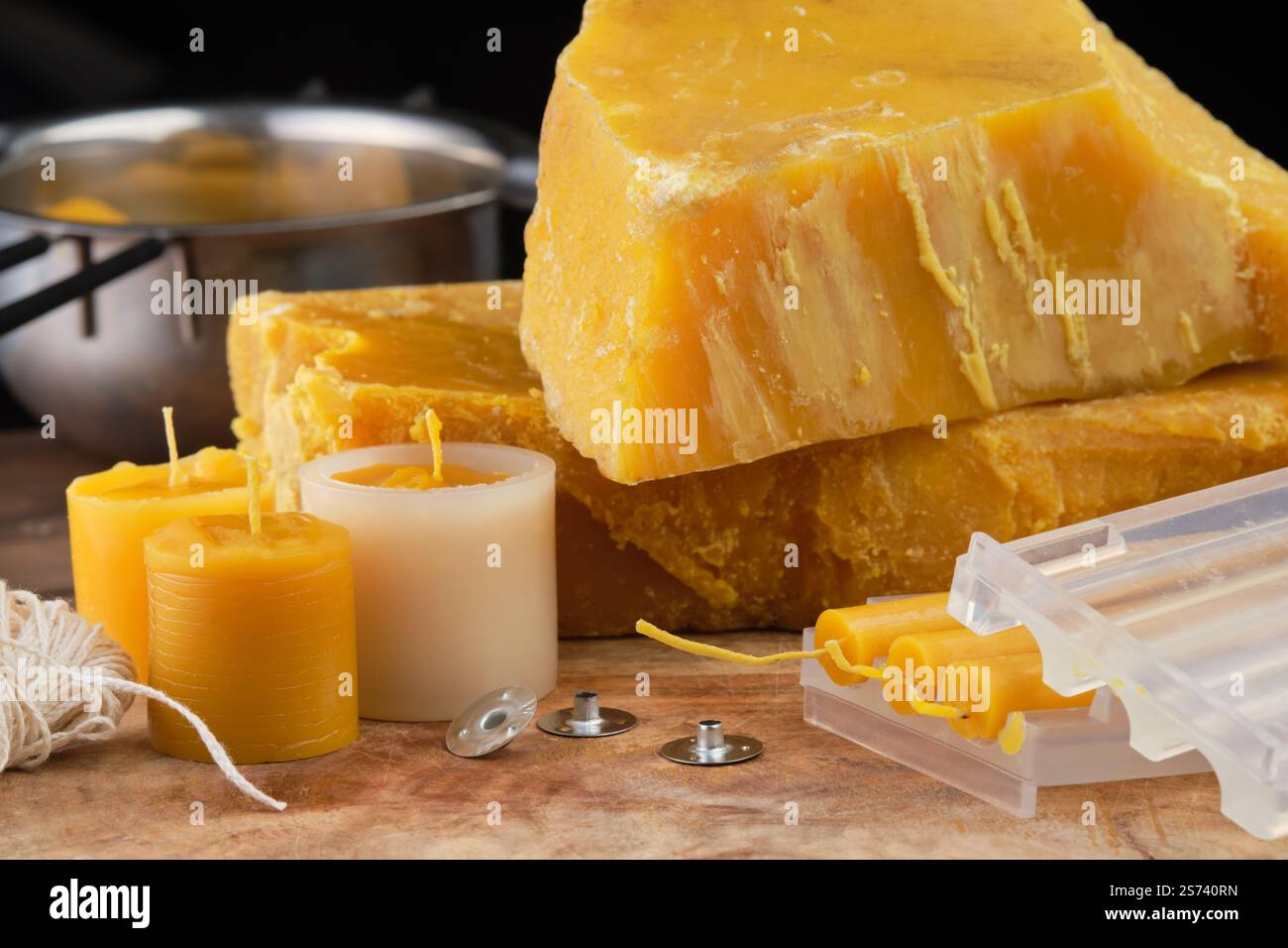 Cera d'api naturale, stampi, stoppini, stoppini metallici, melting pot, coltello e utensili per realizzare candele naturali fatte a mano su una superficie rustica in legno. Foto Stock