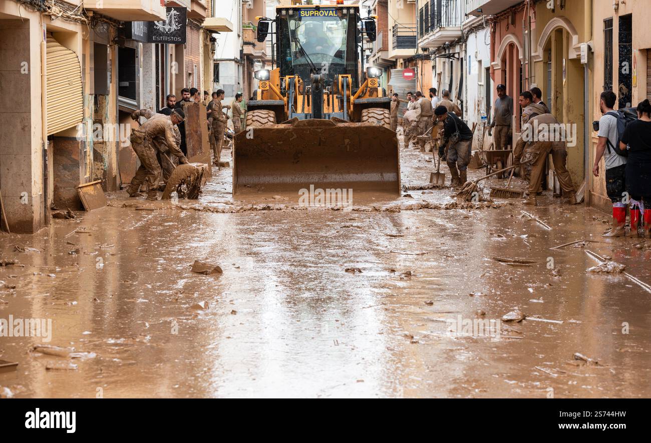 Membri della fanteria dell'esercito spagnolo che aiutano durante le operazioni di pulizia dopo le inondazioni DANA. La strada è inondata di fango. Foto Stock