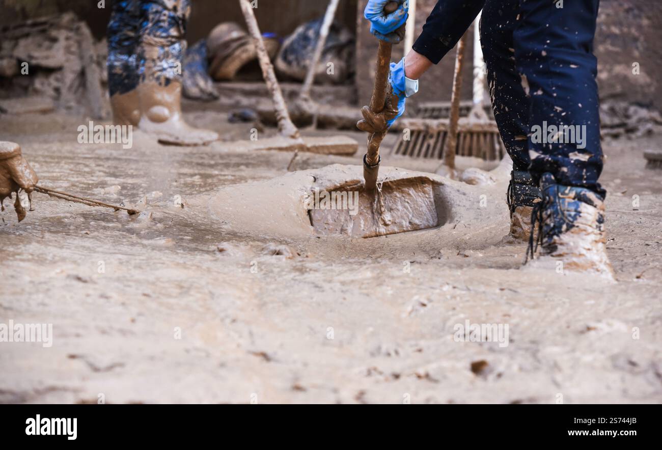 Volontari irriconoscibili che spazzano fango e acqua fangosa in una strada allagata dopo le inondazioni DANA. Massanassa, Spagna. Foto Stock