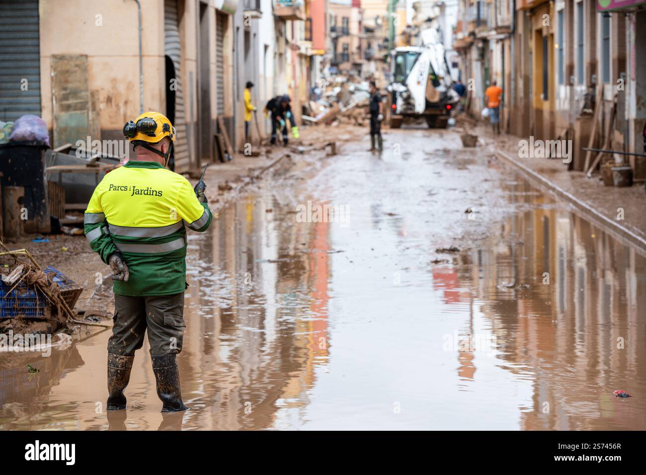 Lavoratore della Comunità Valenciana Generalitat con walkie talkie che supervisiona le operazioni di pulizia nelle strade inondate di fango Foto Stock