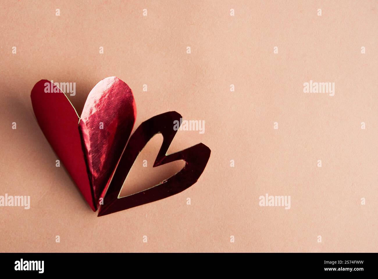 Un cuore in carta rosa riflettente lucido posizionato su uno sfondo rosa coordinato. Foto Stock