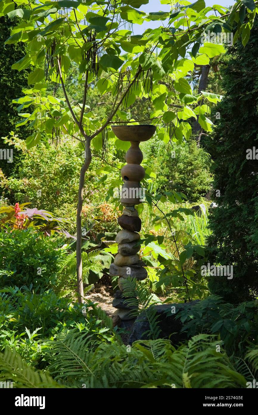 Scultura di rocce piene e vasi di ceramica accanto a Catalpa bungei - albero di Catalpa Manciuria e Pteridophyta - piante di felce nel giardino sul retro in estate, Foto Stock