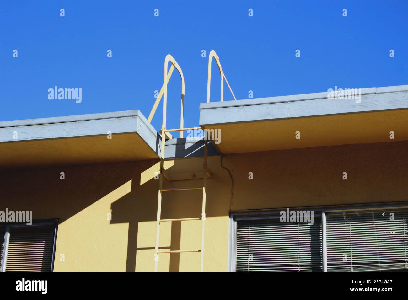 Scala di accesso sul tetto urbana con ringhiere gialle contro un cielo azzurro Foto Stock Scala di accesso sul tetto urbana con ringhiere gialle contro un cielo azzurro Foto Stock