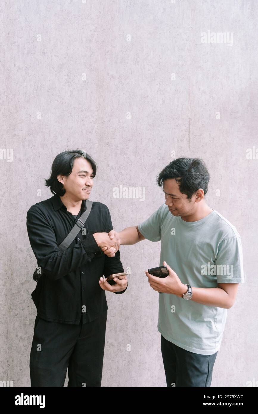 Due uomini stringono la mano dopo aver raggiunto un accordo relativo ai contenuti su un telefono cellulare, simboleggiando il successo della comunicazione e della collaborazione. Foto Stock