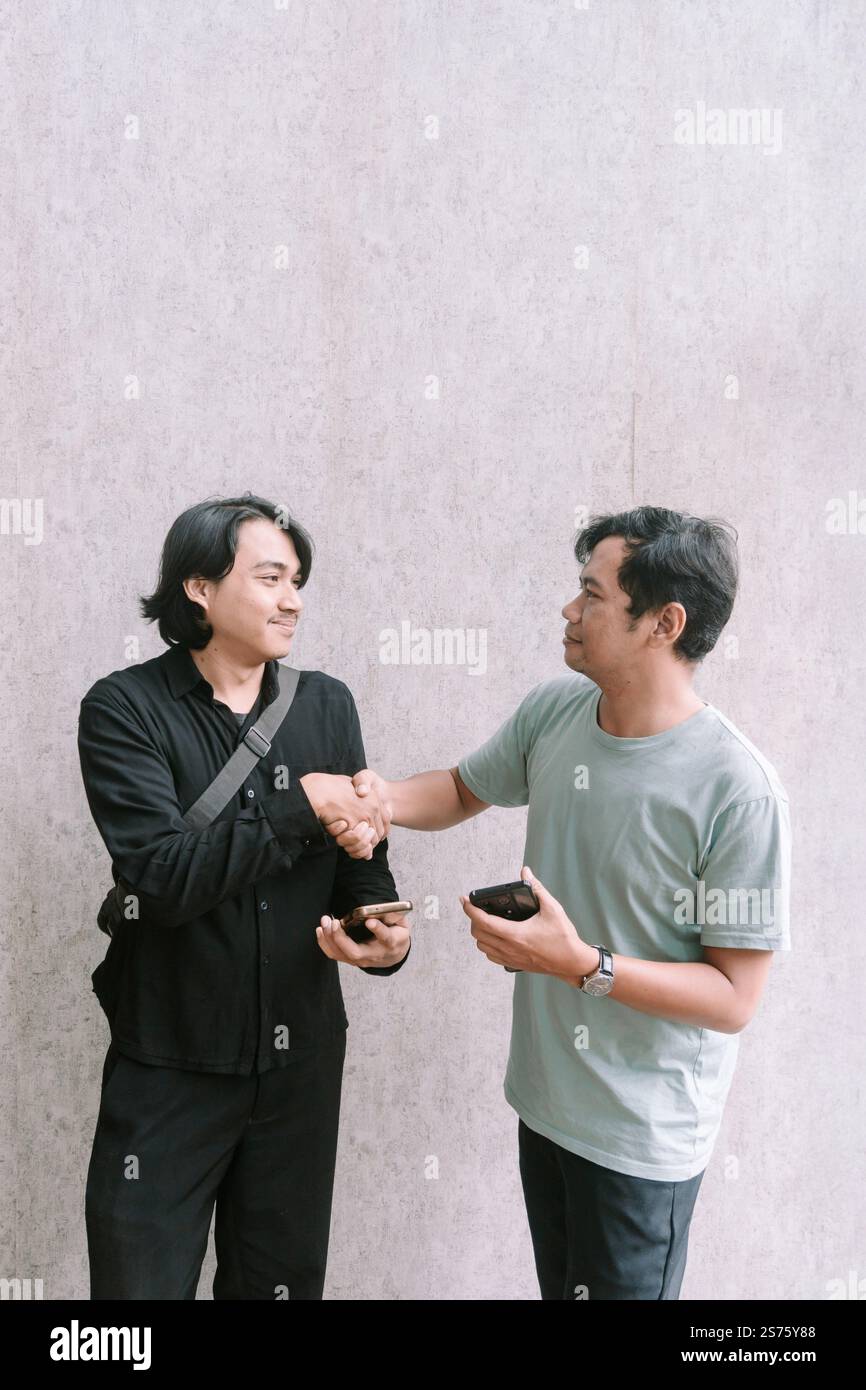 Due uomini stringono la mano dopo aver raggiunto un accordo relativo ai contenuti su un telefono cellulare, simboleggiando il successo della comunicazione e della collaborazione. Foto Stock