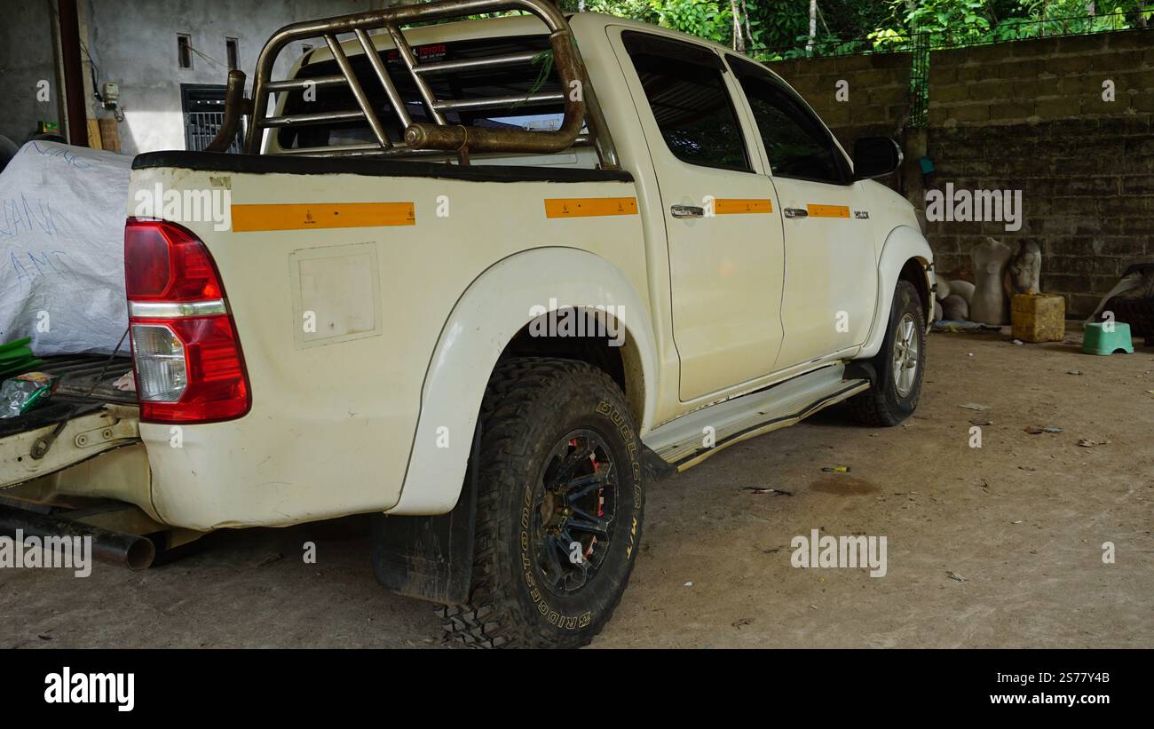 Un pick-up bianco parcheggiato in un garage rustico. Il veicolo è dotato di barra di sicurezza, ruote nere e un po' di usura sulla carrozzeria. Lo sfondo mostra un cemento Foto Stock