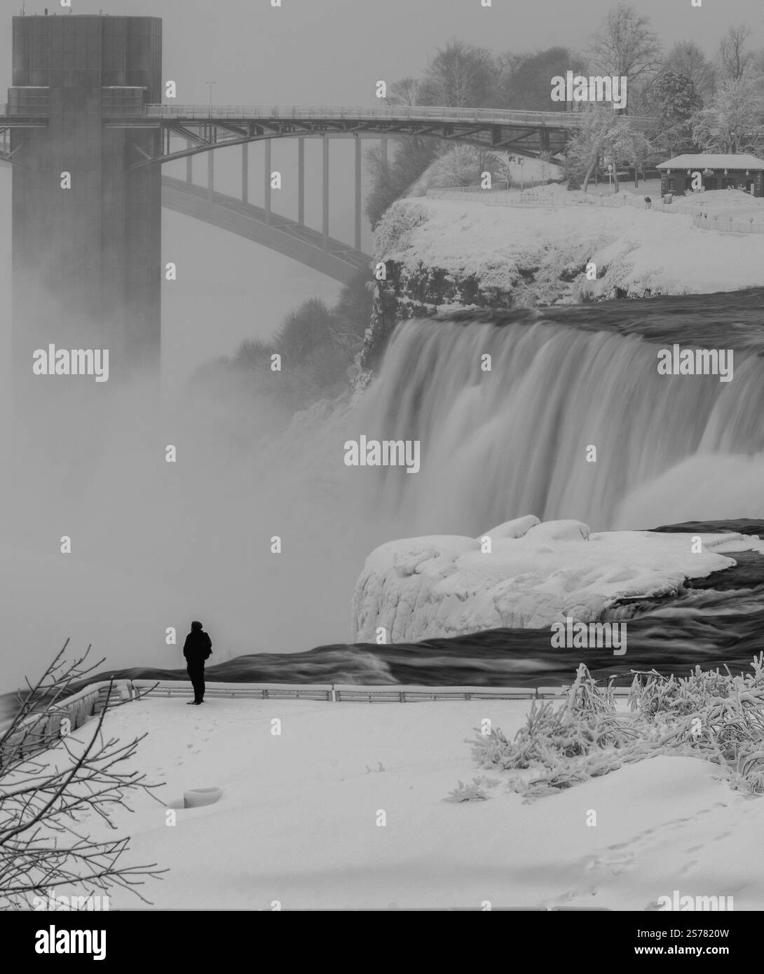 Una fotografia in bianco e nero delle Cascate del Niagara in inverno, con neve, nebbia e una figura solitaria. Catturati con una lunga esposizione per un effetto spettacolare. Foto Stock