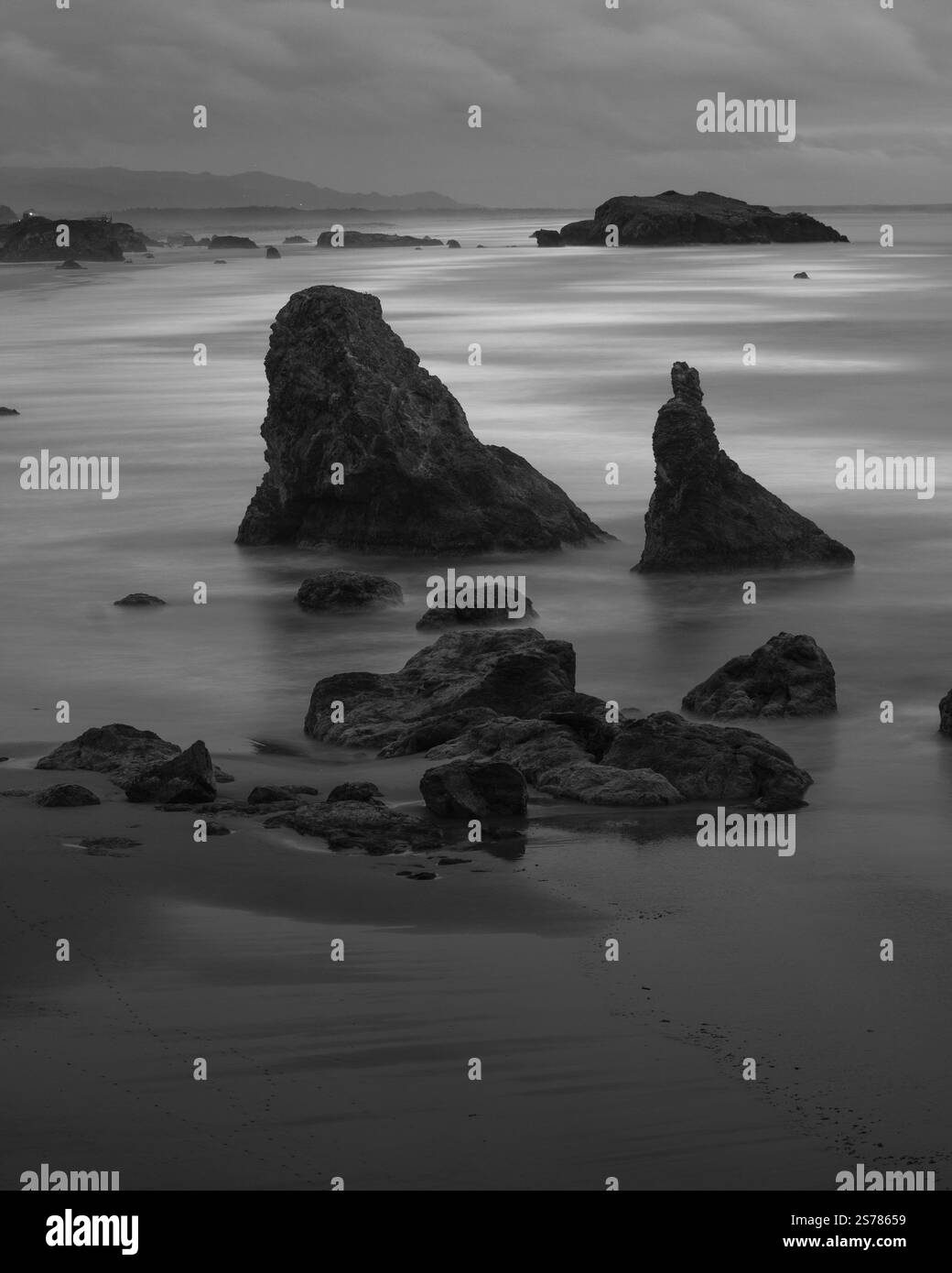 Un paesaggio marino bianco e nero di Bandon Beach, Oregon, caratterizzato da toni moody, fondali marini e un oceano tranquillo catturato con una lunga esposizione. Foto Stock