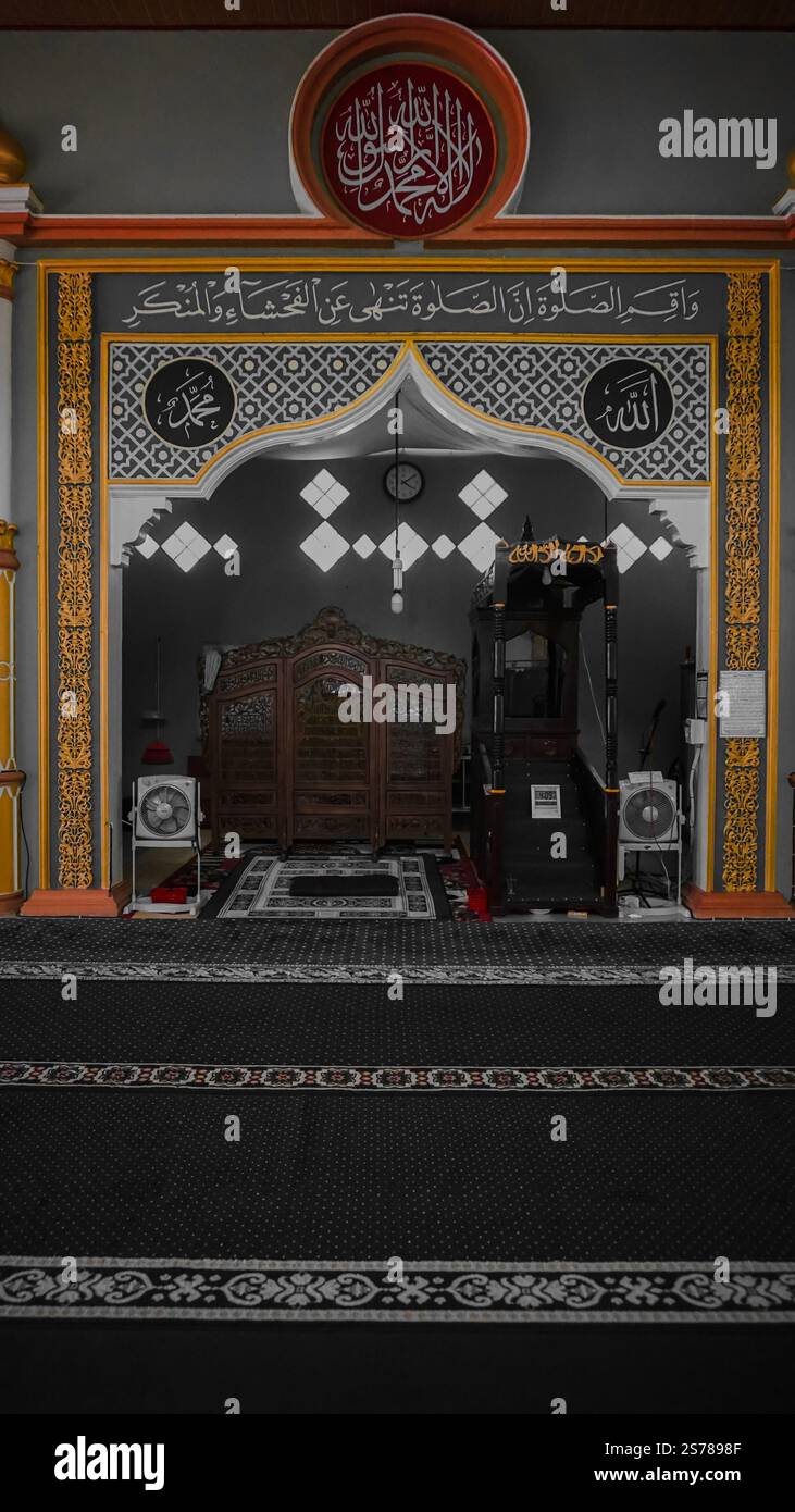 Interno di una moschea caratterizzata da un mihrab decorato con calligrafia araba e motivi decorativi. L'area è adornata da intricati lavori in legno e argilla Foto Stock