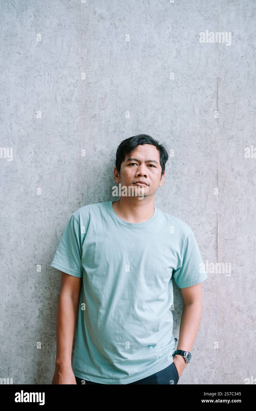Uomo asiatico rilassato in una posa informale su uno sfondo grigio Foto Stock