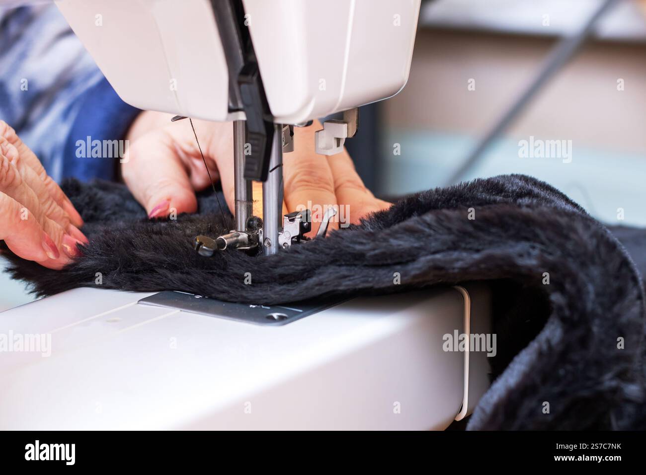 Una donna sta cucendo sapientemente un pezzo di morbida pelliccia nera su una macchina da cucire, dimostrando la sua creatività e il suo talento nella lavorazione Foto Stock