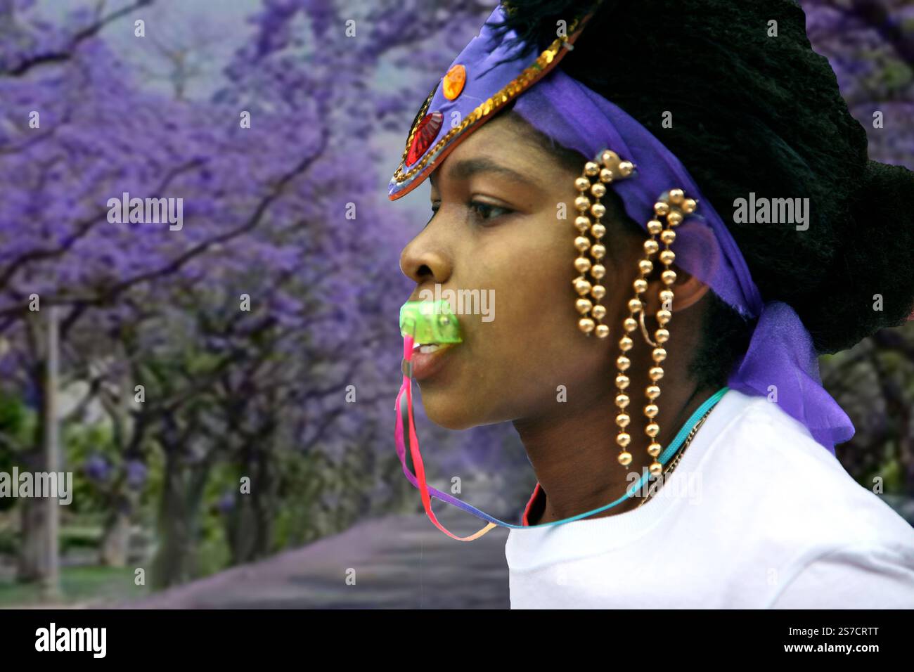 Un fischietto di una Mas Band al Carnevale di Hackney, che mostra le tradizioni culturali. L'archetto con perline si fonde con un vivace sfondo di alberi viola. Foto Stock Un fischietto di una Mas Band al Carnevale di Hackney, che mostra le tradizioni culturali. L'archetto con perline si fonde con un vivace sfondo di alberi viola. Foto Stock
