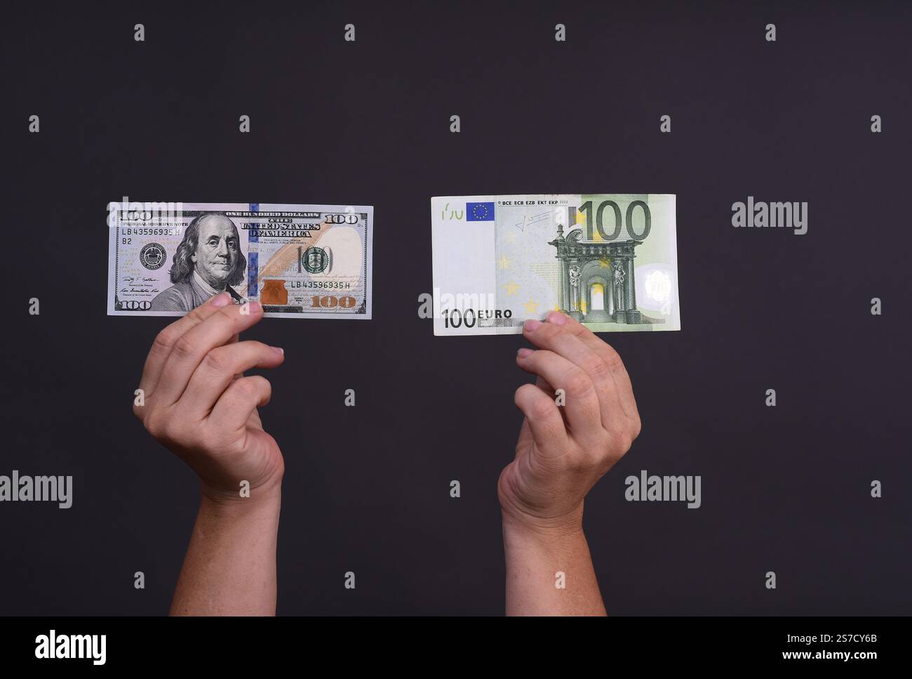 banconota da cento euro e cento dollari in mano su sfondo grigio. primo piano Foto Stock