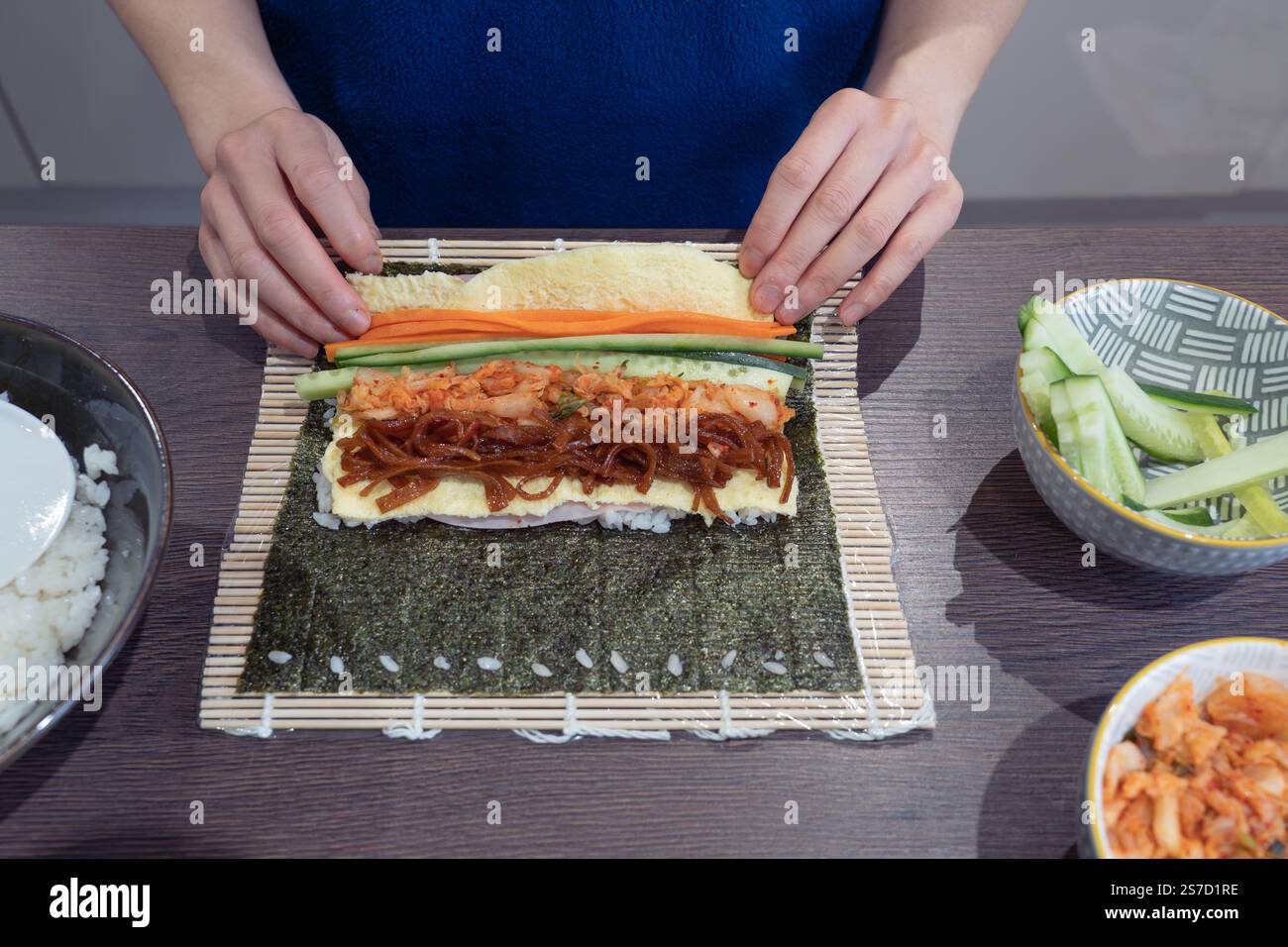 Donna asiatica che rotola un Kimchi Gimbap usando il tappetino di bambù sotto. Il Gimbap è un piatto sudcoreano. Tema: Cucina asiatica, cucina coreana, cucina casalinga Foto Stock