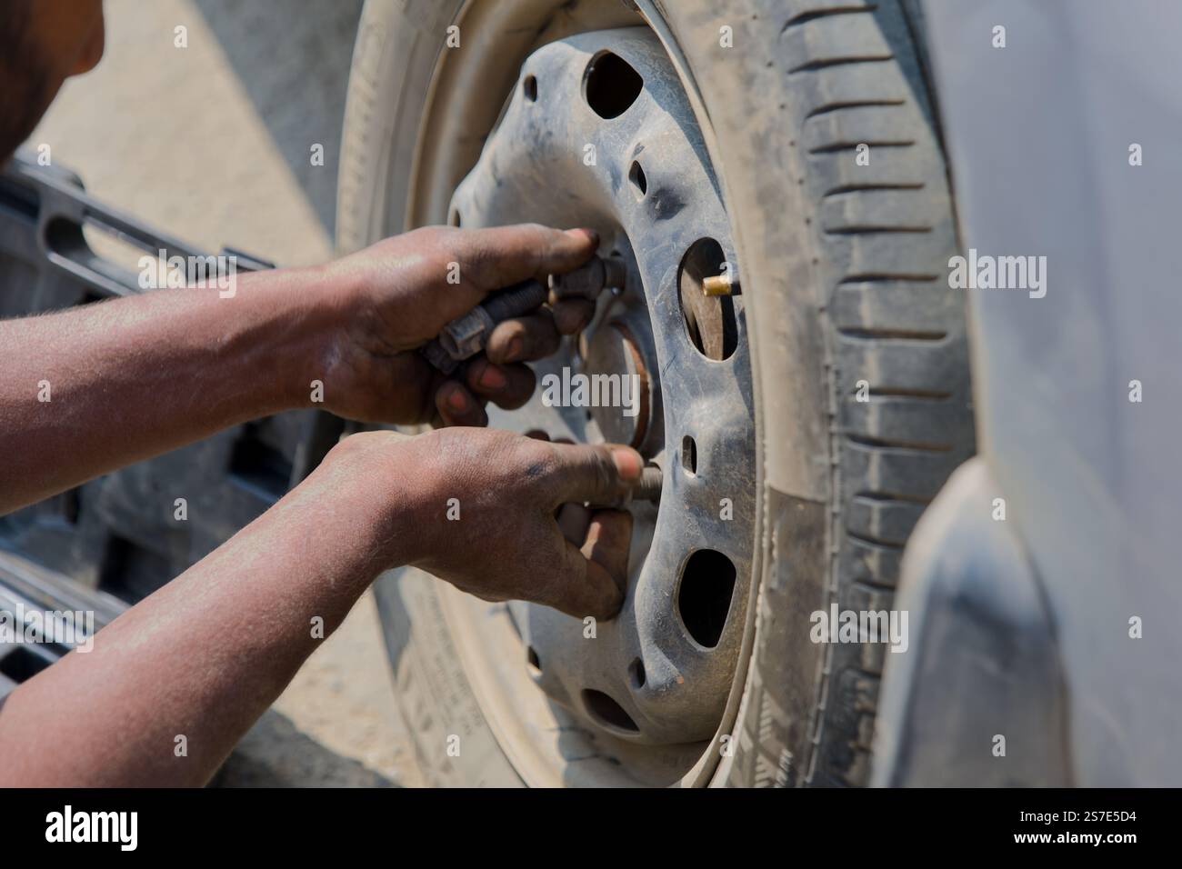 Questa immagine cattura una vista ravvicinata delle mani di una persona che lavora su uno pneumatico di un'auto utilizzando uno strumento. Lo pneumatico e la ruota sono sporchi Foto Stock