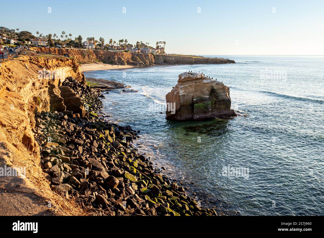 La luce dorata del tramonto esalta la bellezza delle Sunset Cliffs e della roccia di Ross, evidenziando la costa frastagliata e la spiaggia tranquilla Foto Stock