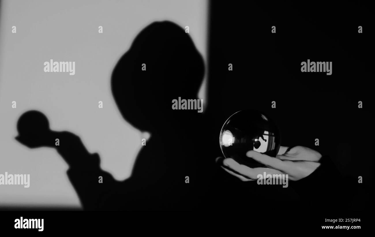 fotografia artistica in bianco e nero con una figura ombrosa che regge una sfera di vetro riflettente. Foto Stock