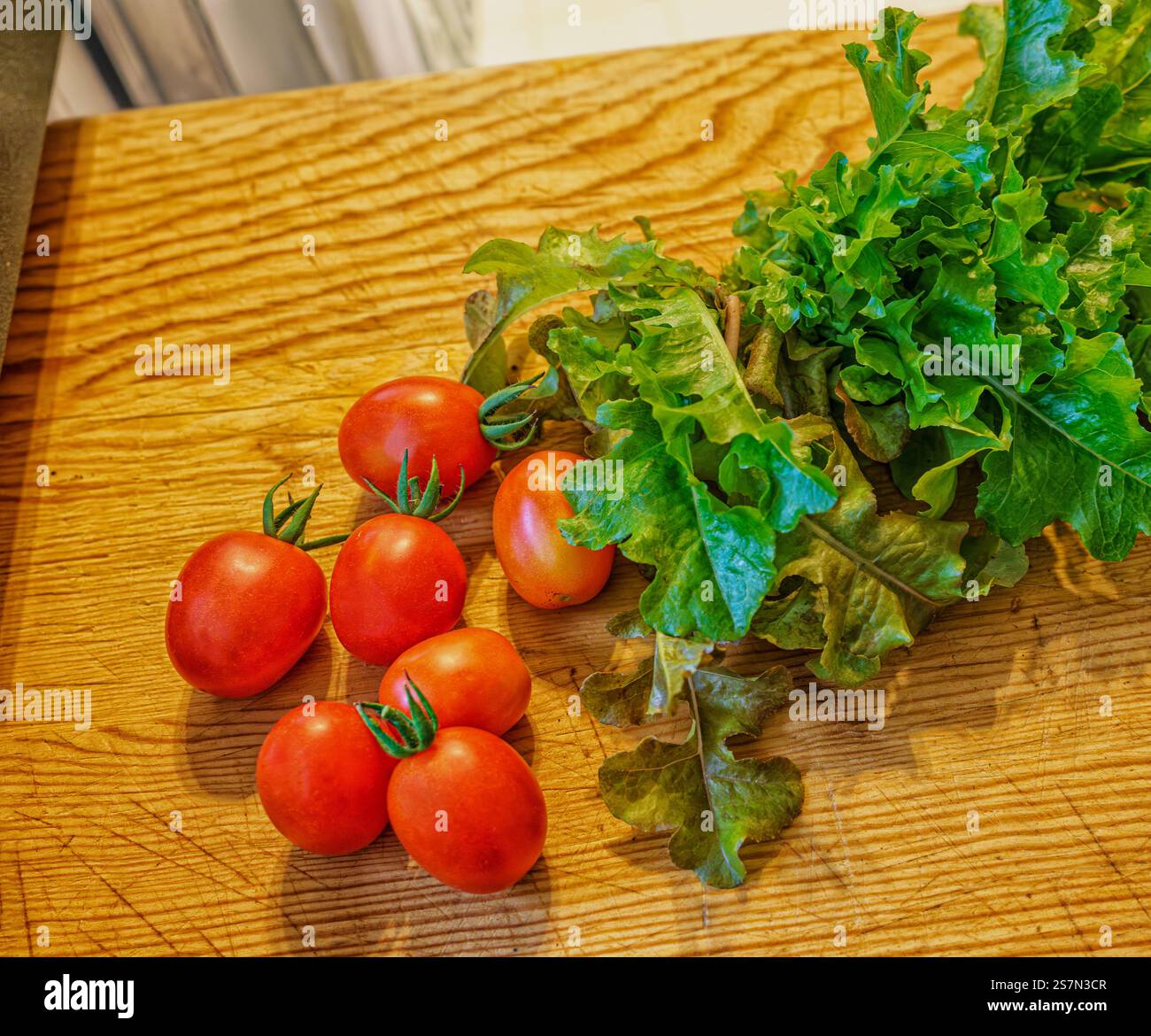 Prodotti biologici appena raccolti in casa, ingredienti salutari per insalate pomodori d'uva e lattuga mix primaverile su un tagliere di legno. Foto Stock
