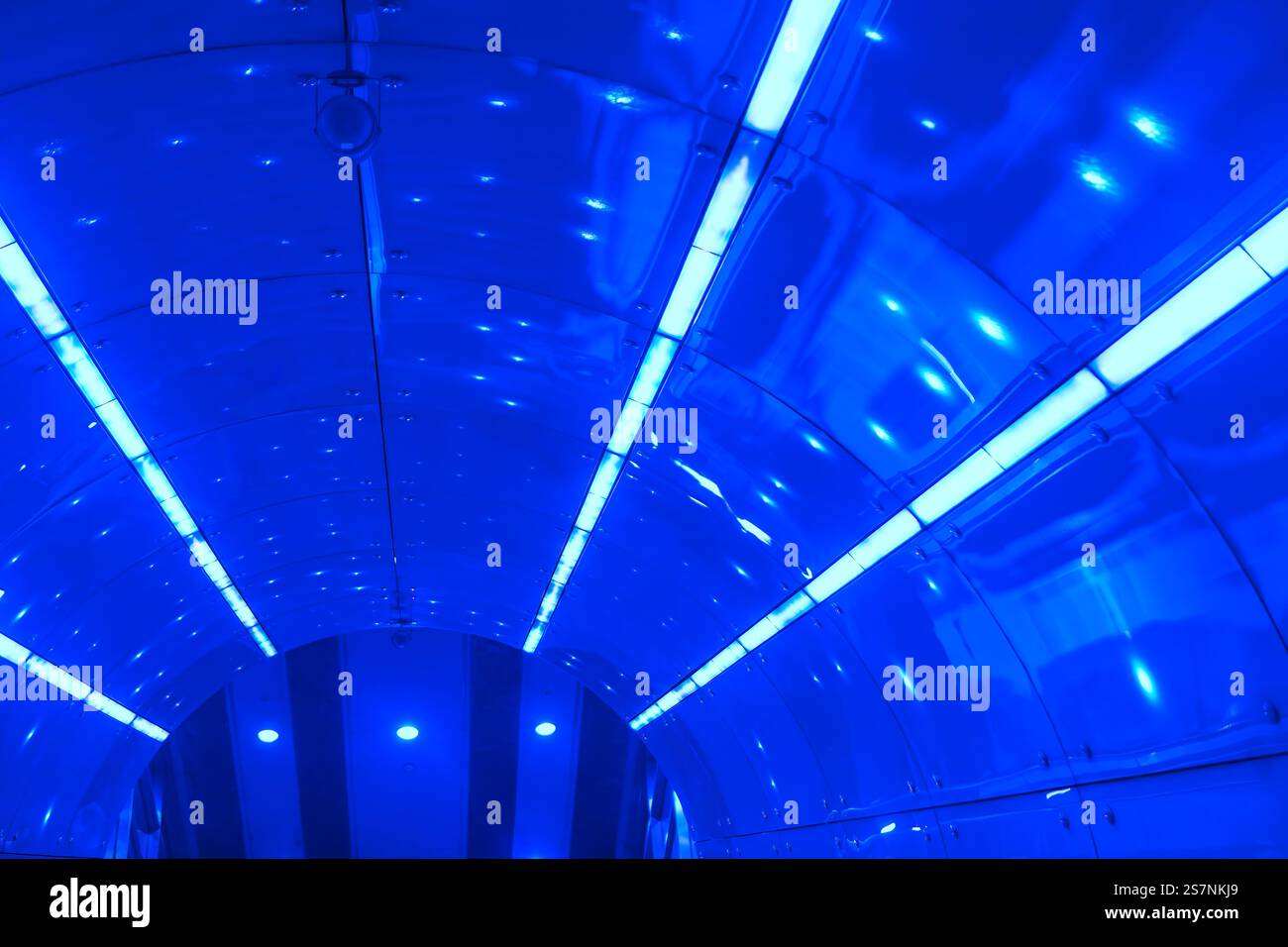 Interno di un tunnel o di un passaggio con soffitto curvo realizzato con pannelli metallici riflettenti. Il soffitto è rivestito di luci fluorescenti che creano un m Foto Stock