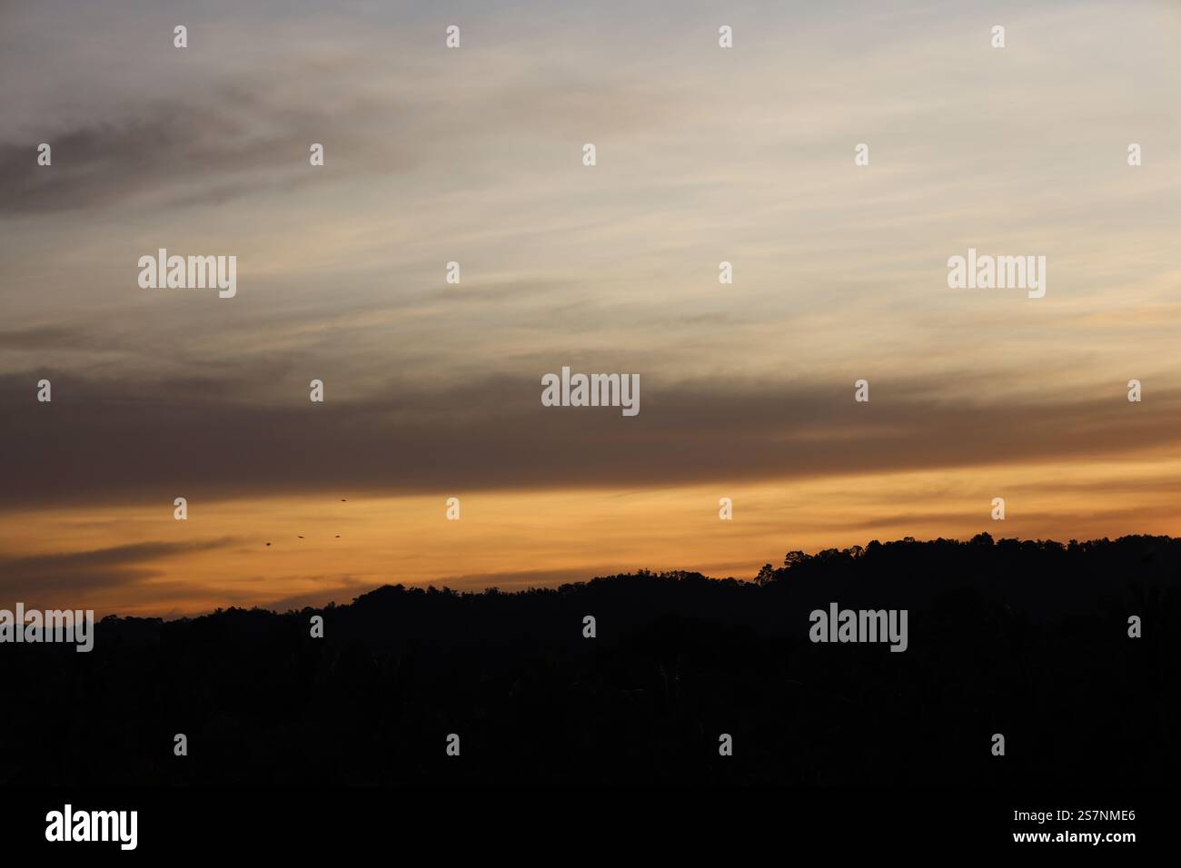 basse nuvole blu e grigio scuro pendenti si stendono in basso sopra le colline coperte dalla foresta pluviale mentre l'alba si avvicina Foto Stock