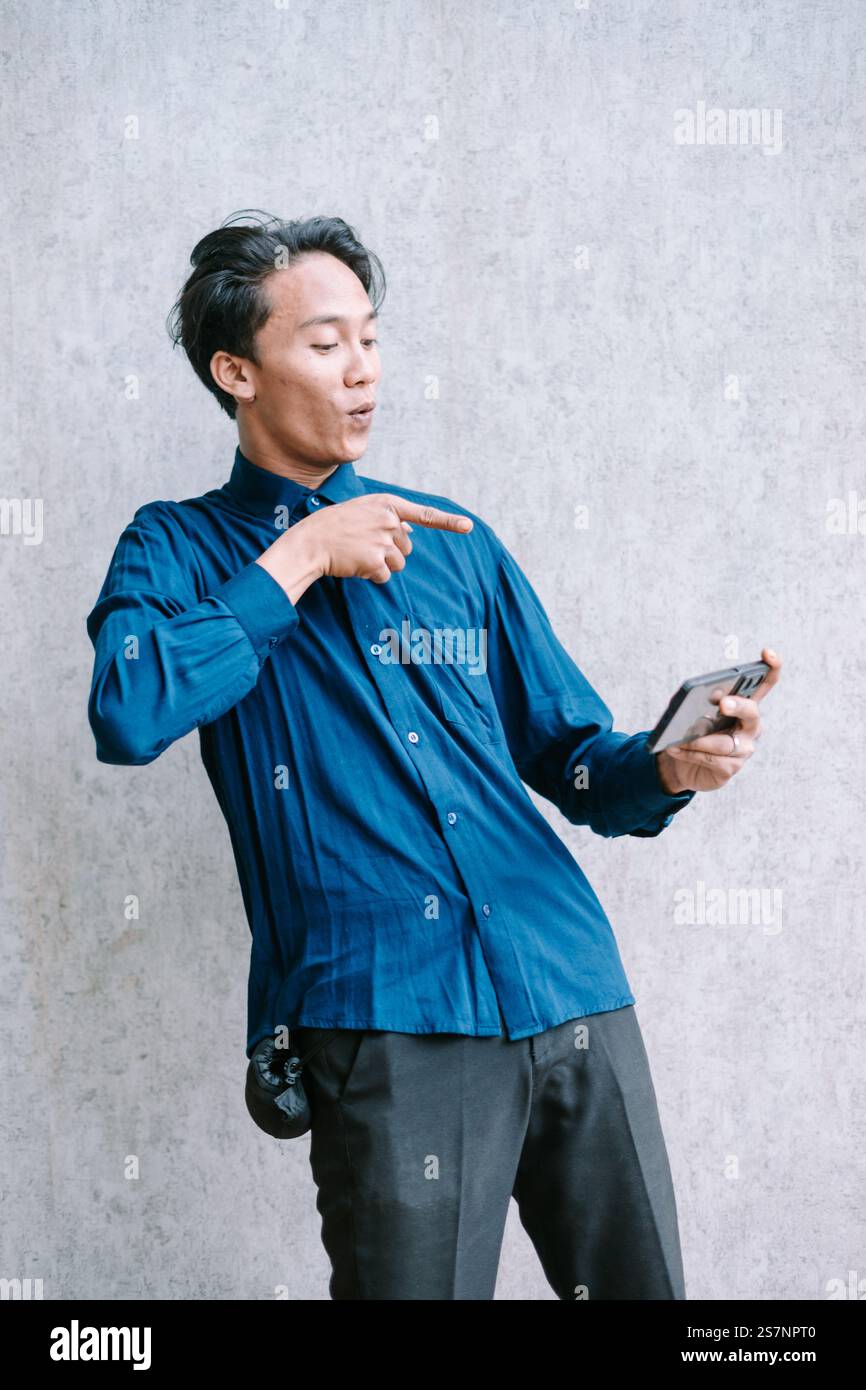 Giovane eccitato che punta al suo telefono, condividendo contenuti interessanti. Foto Stock
