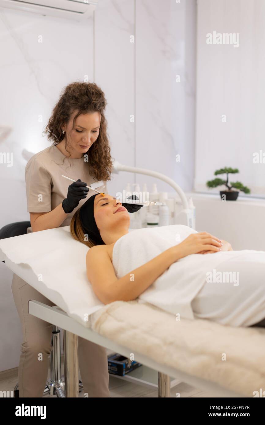 In una serena sala spa, un estetista esperto applica il retinolo sierico a un cliente rilassato, concentrandosi sul ringiovanimento della sua pelle per un bagliore giovanile Foto Stock