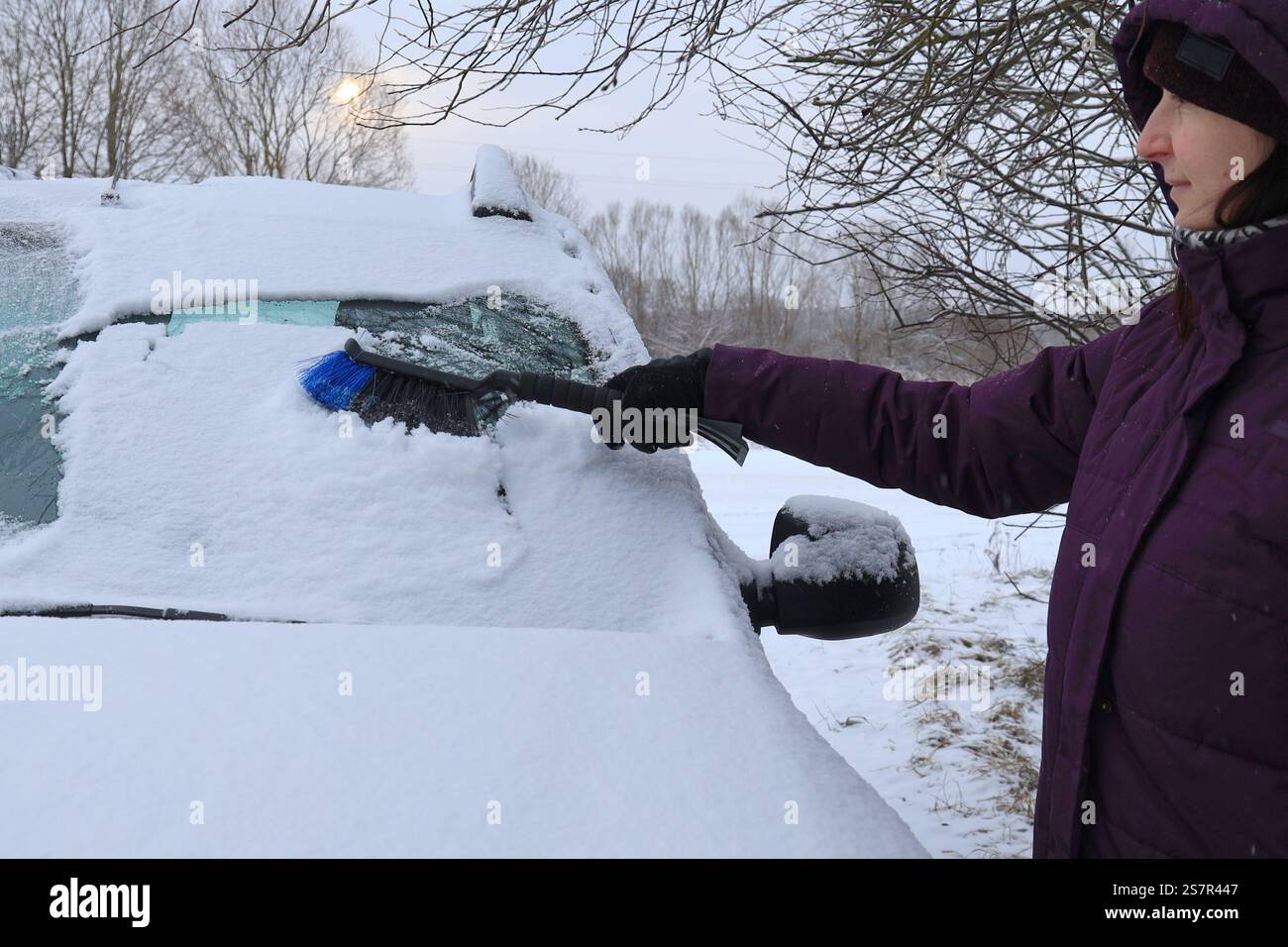 La proprietaria di un'auto pulisce la neve dal parabrezza dell'auto con una spazzola per auto durante il primo piano del giorno di sole Foto Stock
