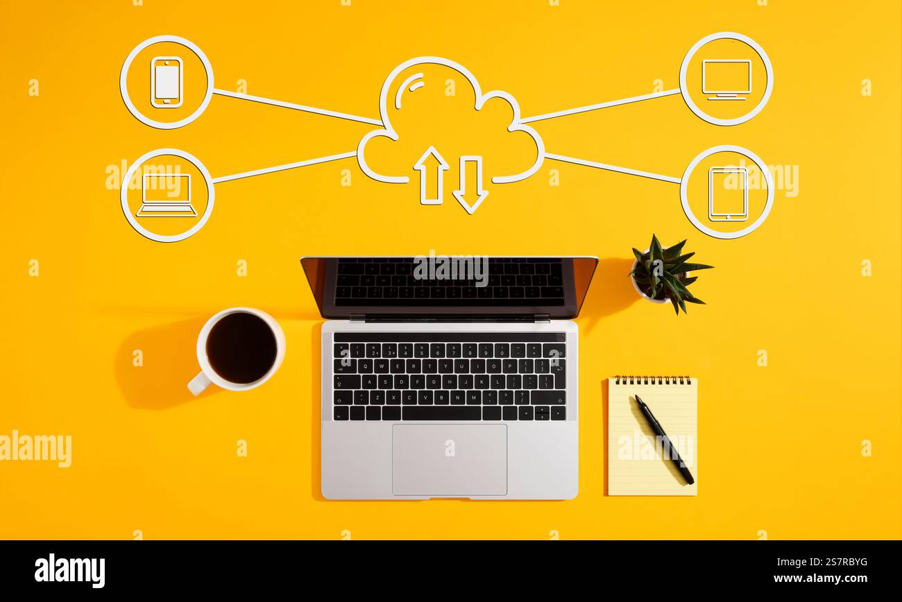 Diagramma di cloud computing che mostra lo scambio di dati tra laptop, smartphone, tablet e computer su sfondo giallo, con caffè, blocco note e penna Foto Stock