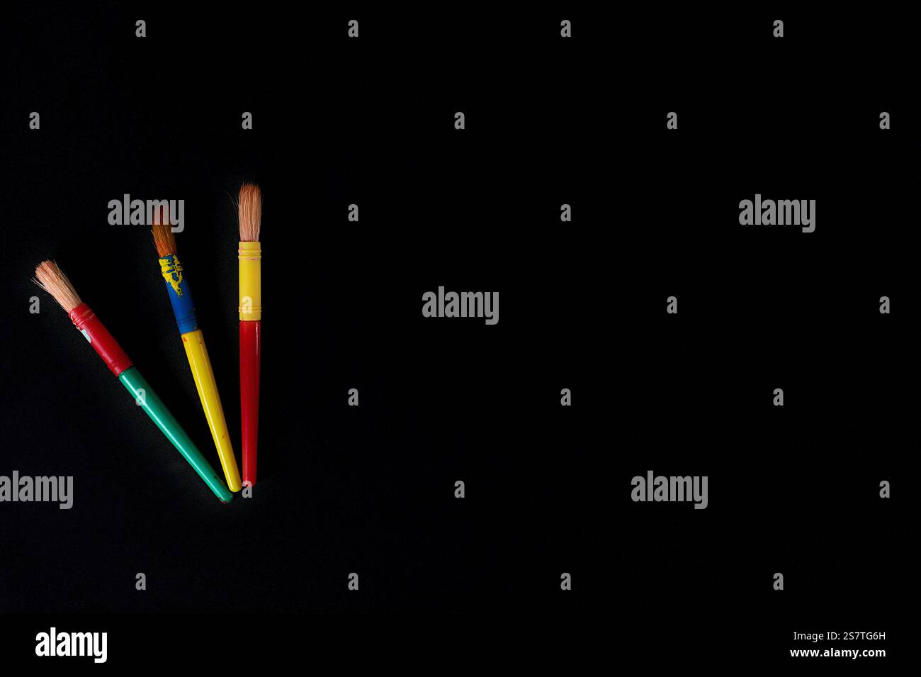 Tre pennelli vivaci si distinguono su uno sfondo scuro, a simboleggiare la creatività e l'espressione artistica. Foto Stock