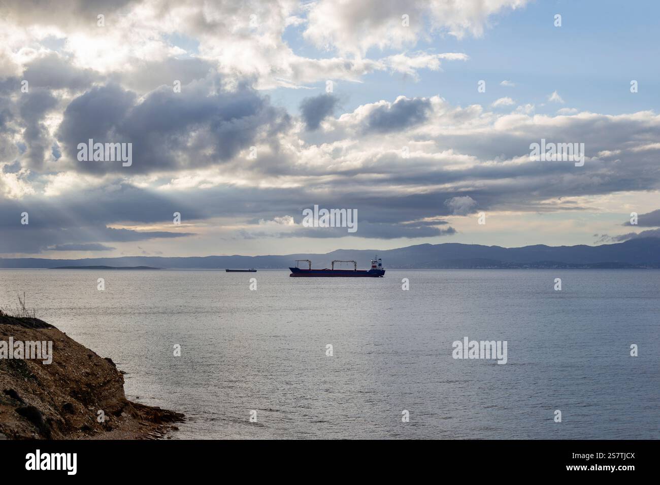 Barca a vela nel mare egeo con cielo nuvoloso e spiaggia rocciosa Foto Stock