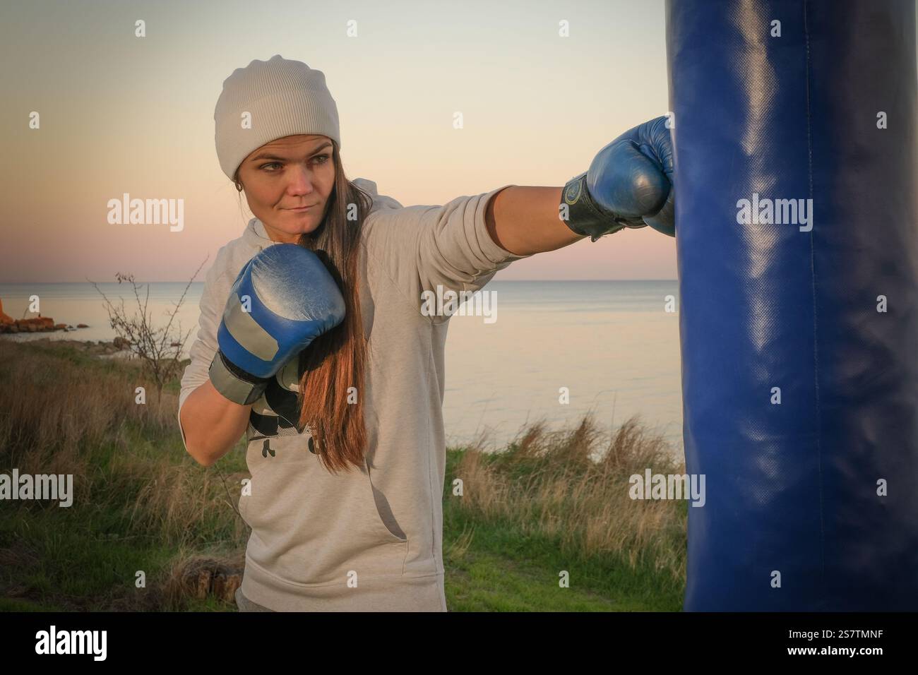 Donna pugilato con i guanti e la borsa perforatrice sulla riva del mare la sera Foto Stock