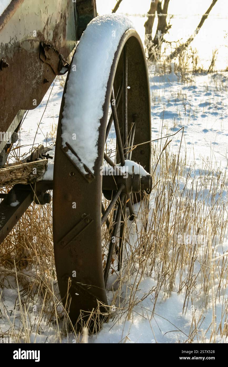 Una ruota arrugginita con neve sopra. La ruota è vecchia e arrugginita ed è circondata dalla neve. La neve copre la ruota e il terreno, creando un pe Foto Stock
