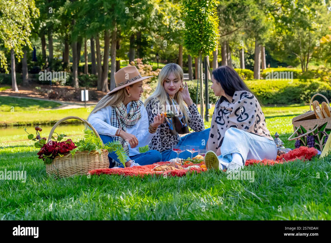 Tre belle donne europee si siedono su una coperta, condividendo risate e pensieri sotto alberi d'autunno dorati. Circondati da foglie vibranti, si godono il foo Foto Stock