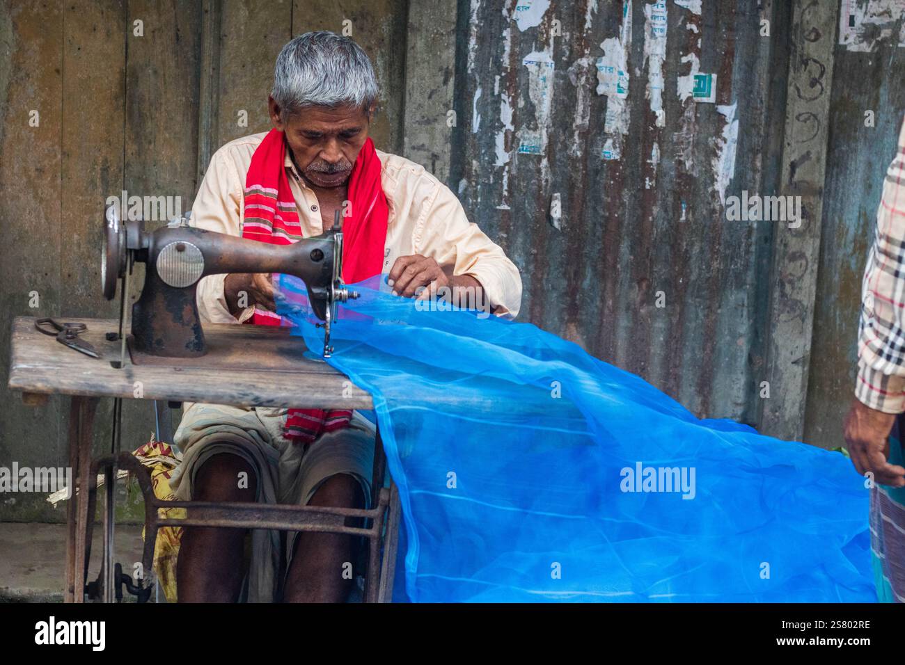 Cumilla, Bangladesh - 24 ottobre 2023: Un vecchio che cucisce tessuti in un negozio di strada che sarta il mercato locale. Foto Stock Cumilla, Bangladesh - 24 ottobre 2023: Un vecchio che cucisce tessuti in un negozio di strada che sarta il mercato locale. Foto Stock