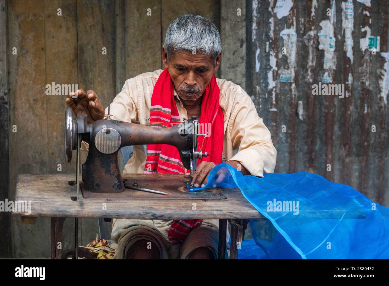 Cumilla, Bangladesh - 24 ottobre 2023: Un vecchio che cucisce tessuti in un negozio di strada che sarta il mercato locale. Foto Stock Cumilla, Bangladesh - 24 ottobre 2023: Un vecchio che cucisce tessuti in un negozio di strada che sarta il mercato locale. Foto Stock