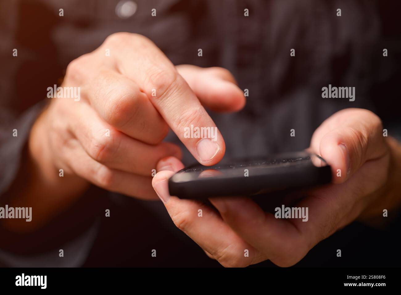 Primo piano di mani maschili utilizzando il telefono cellulare in una stanza buia, uomo che digita un messaggio di testo sullo smartphone, messa a fuoco selettiva Foto Stock