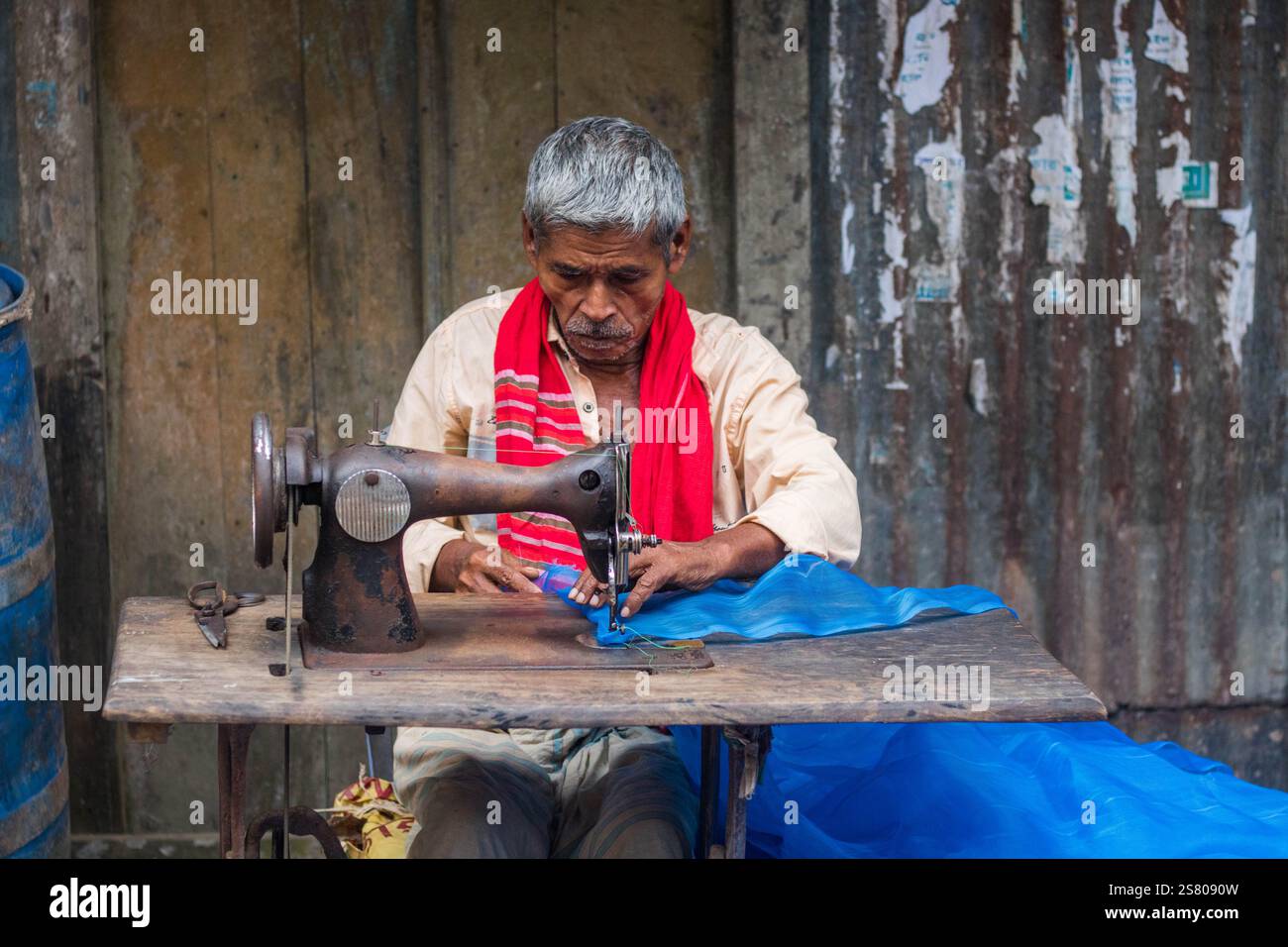Cumilla, Bangladesh - 24 ottobre 2023: Un vecchio che cucisce tessuti in un negozio di strada che sarta il mercato locale. Foto Stock Cumilla, Bangladesh - 24 ottobre 2023: Un vecchio che cucisce tessuti in un negozio di strada che sarta il mercato locale. Foto Stock
