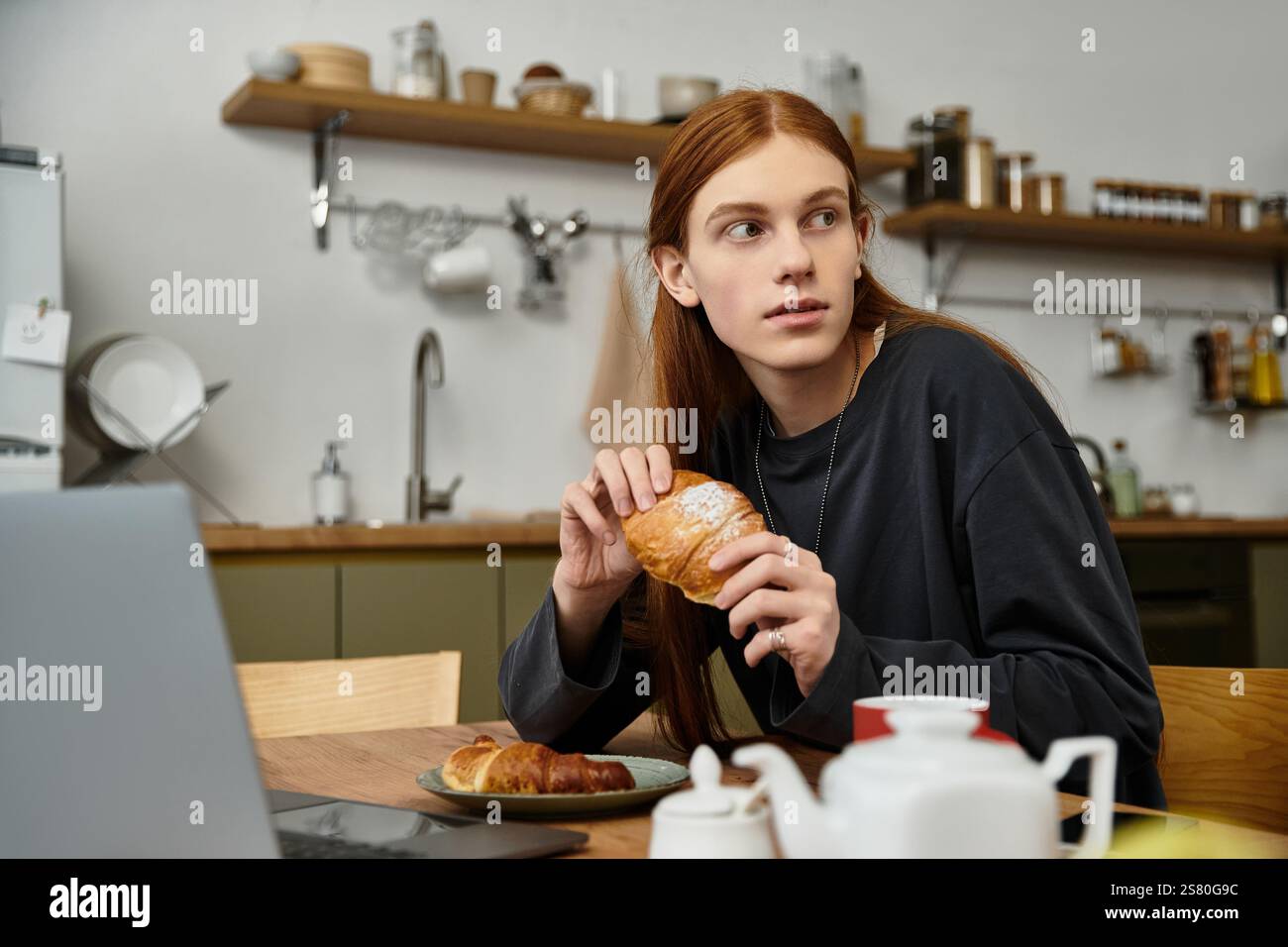 L'atmosfera informale del mattino riempie l'aria mentre un giovane assapora una deliziosa pasticceria a casa. Foto Stock
