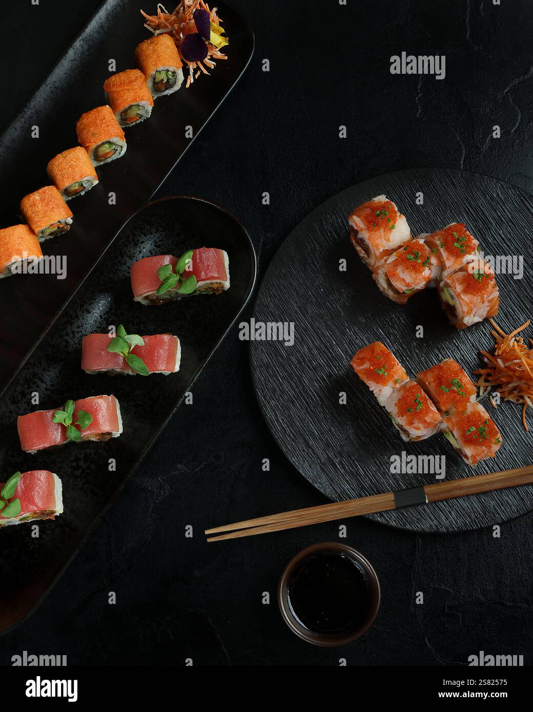 Un elegante piatto di sushi con una varietà di panini, tra cui piatti piccanti, tonni e salmoni, disposti su piatti neri con decorazioni e croccanti Foto Stock