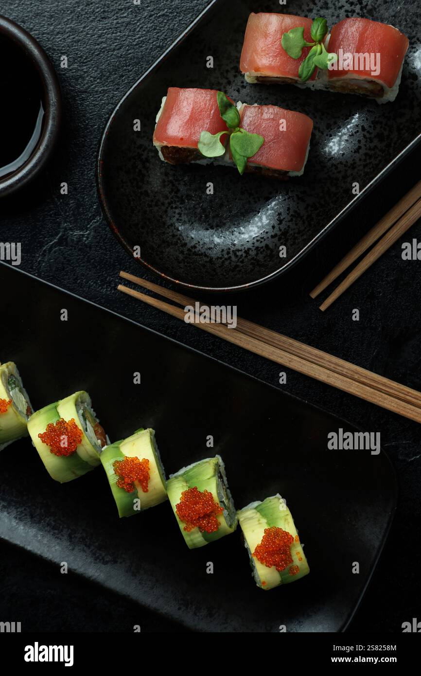 Un elegante piatto di sushi con una varietà di panini su piatti neri con guarnigioni e bacchette poste accanto a una ciotola di salsa di soia. Foto Stock