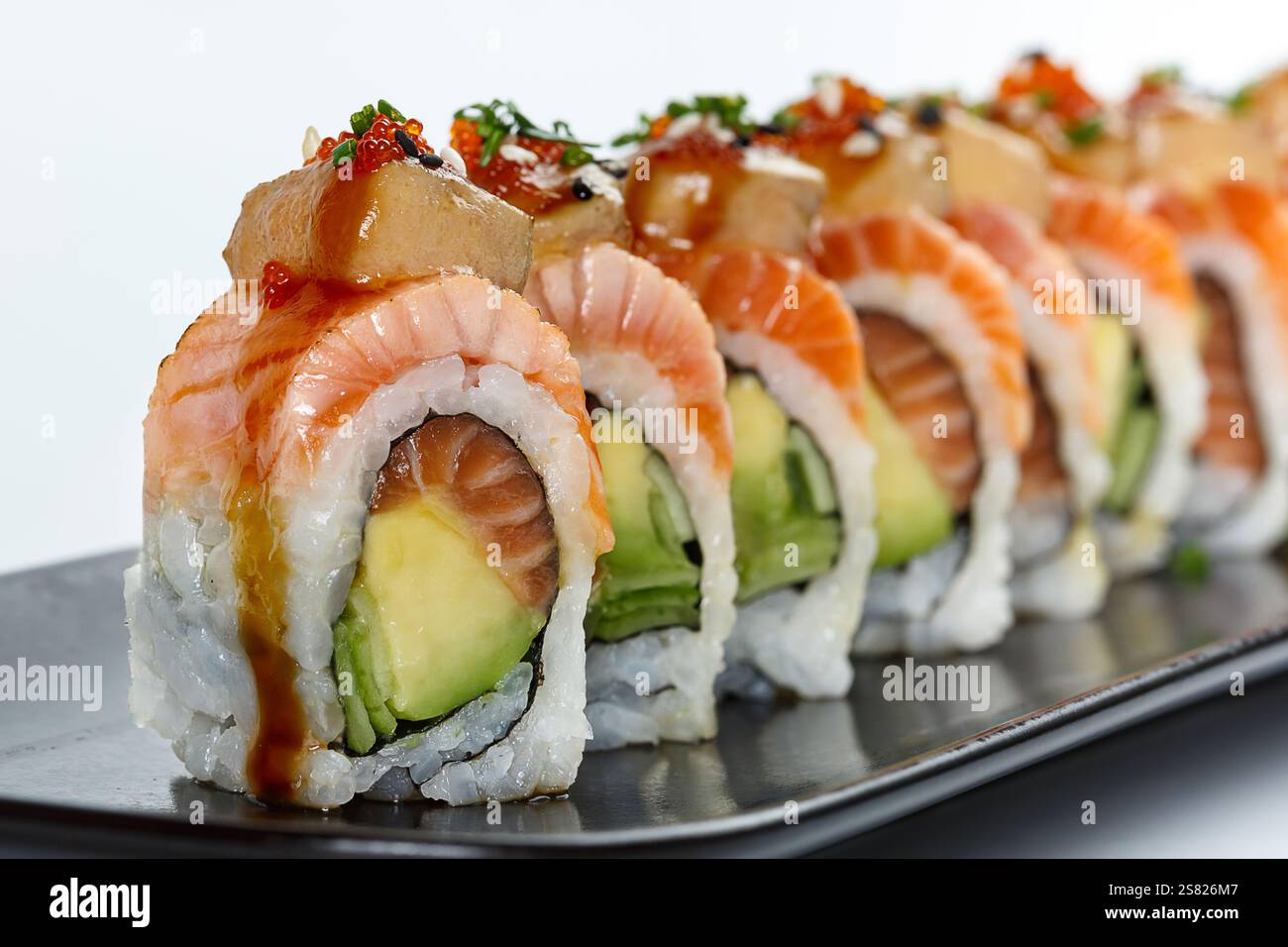 Un sushi roll ben placcato con strati di salmone fresco, avocado, cetrioli e riso, condito con foie gras, caprioli di pesce e condito con saporito sa Foto Stock