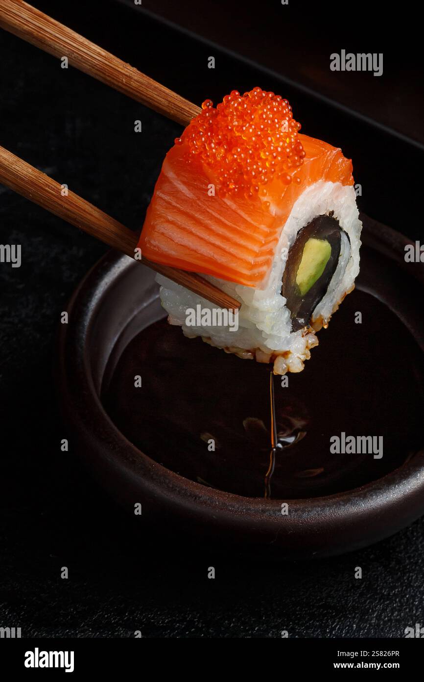 Un sushi roll con salmone fresco e capriolo di pesce è delicatamente tenuto da bacchette, immersi in salsa di soia, mostrando una perfetta armonia di sapori a. Foto Stock