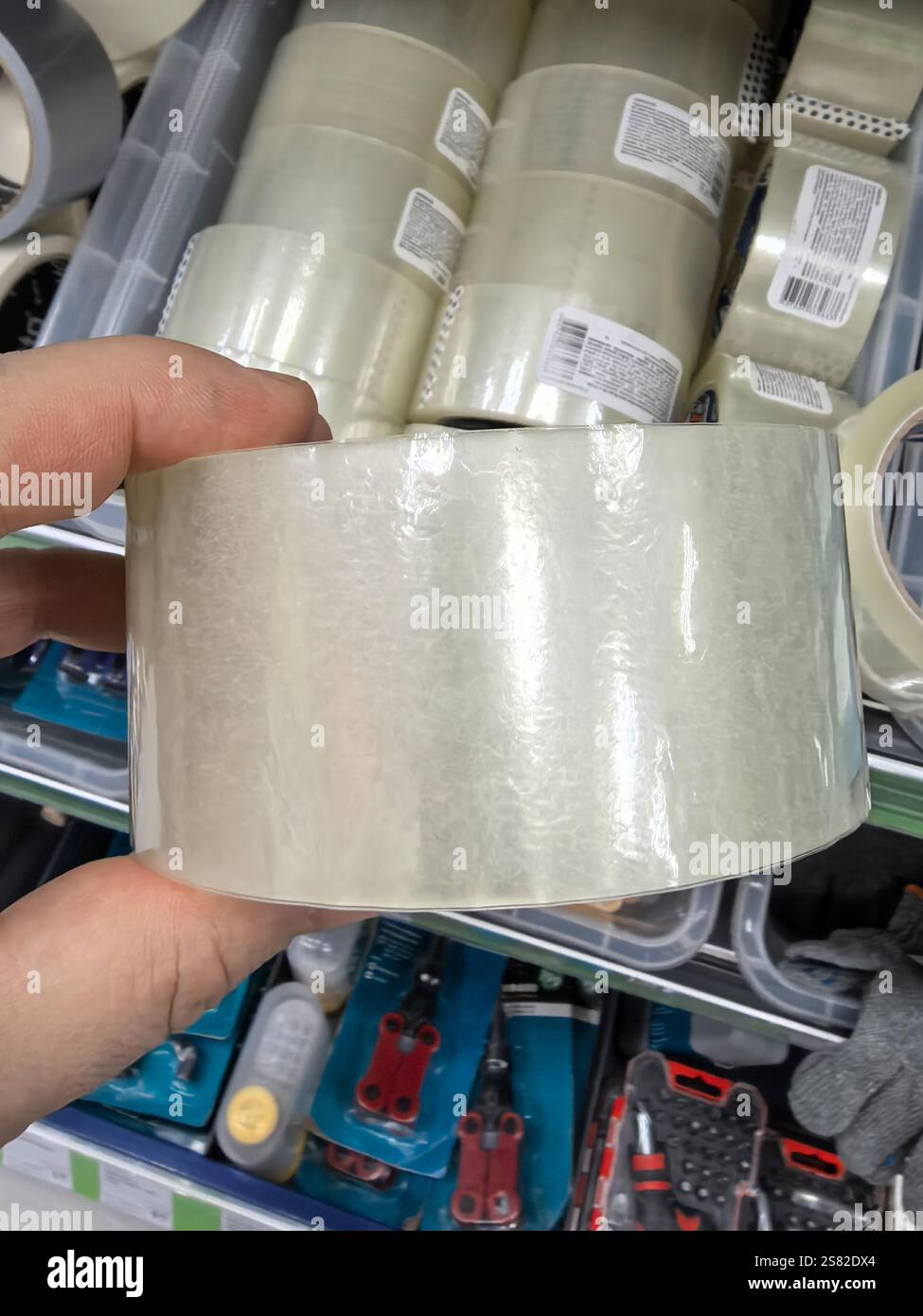 Una persona sta afferrando un rotolo di nastro trasparente mentre si trova in un corridoio ben rifornito di forniture per la lavorazione. Su sono visibili vari strumenti e accessori Foto Stock