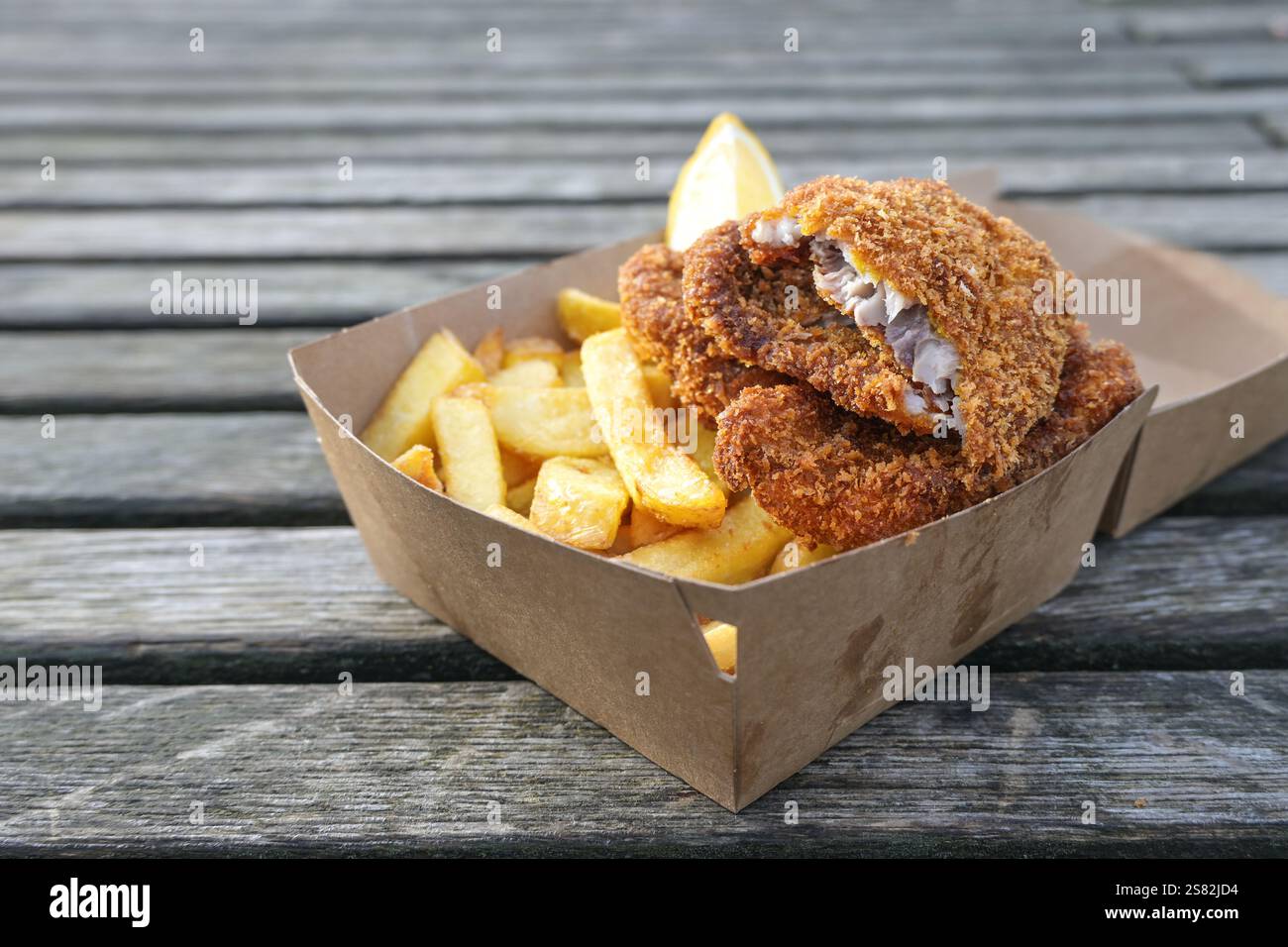 Fish and chips in una scatola di cartone su un molo di legno intemprato nel porto, tradizionale spuntino a base di pesce sulla costa, spazio copia, vista dall'alto, se Foto Stock