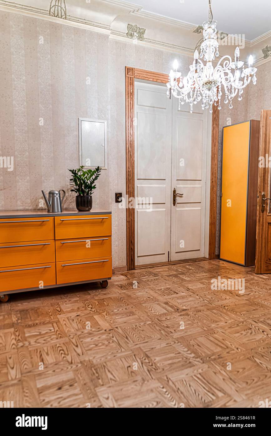 Spazio interno caratterizzato da pavimento in parquet in legno, carta da parati a righe, mobili arancioni, una doppia porta bianca e un lampadario di cristallo. Foto Stock